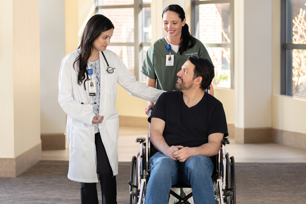 hospital transport staff wheeling patient in wheelchair down hallway