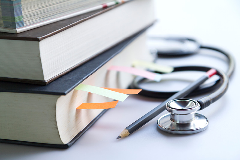 stack of books with marked pages and a pencil and stethoscope