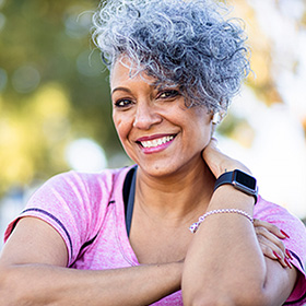 an older woman of color with gray curly hair, wearing a pink athletic shirt and smiling for the camera
