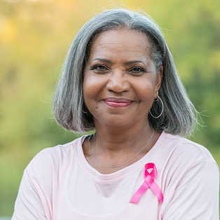 a woman of color with gray hair, wearing pink and smiling at the camera