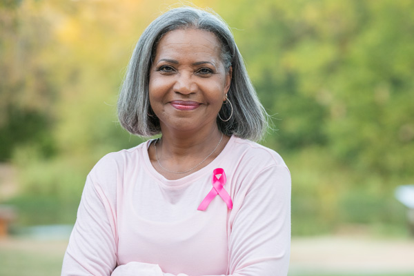 a woman of color with gray hair, wearing pink and smiling at the camera
