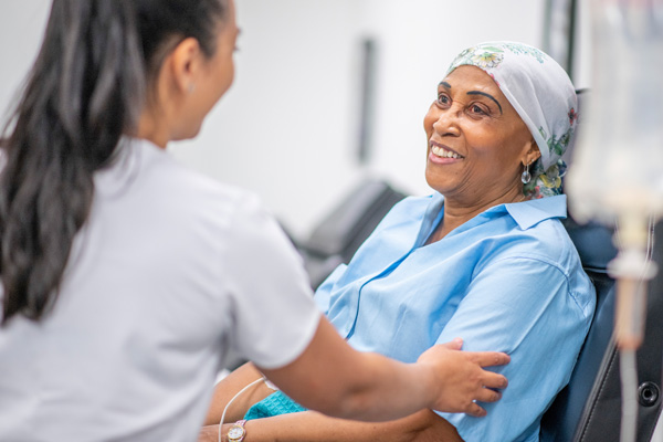 a smiling chemo patient in a chair with a doctor gently touching her arm
