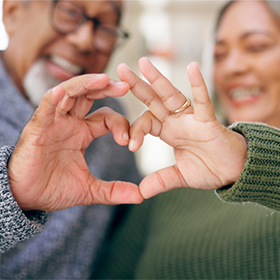 an older couple making a heart with their hands to celebrate Heart Month