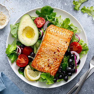 grilled salmon fish fillet and fresh vegetable salad with tomato, red onion, black olives and avocado
