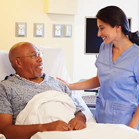 an older man in a hospital gown in a hospital bed being comforted after surgery by a doctor wearing scrubs