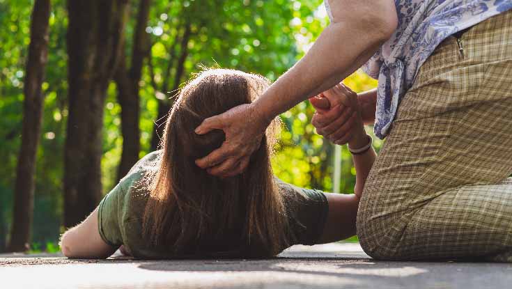 stroke first aid: person holding a woman' head while she is lying on the ground