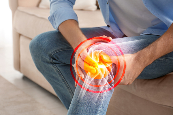 man with knee pain sitting and holding knee