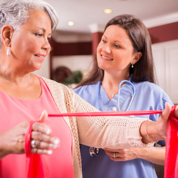 a nurse observing an older person using a stretch band during physical rehab